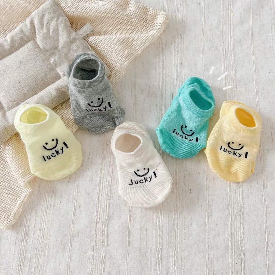 Set of colorful baby socks with smiley faces and 'lucky!' text on a light wooden surface.