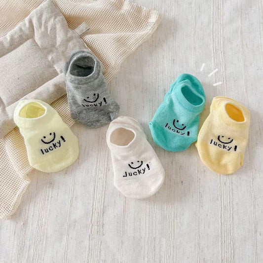 Set of colorful baby socks with smiley faces and 'lucky!' text on a light wooden surface.